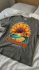 Getaway Sunflower Beach Tee – Pepper displayed on a bed, showcasing vibrant sunflower and coastal design.