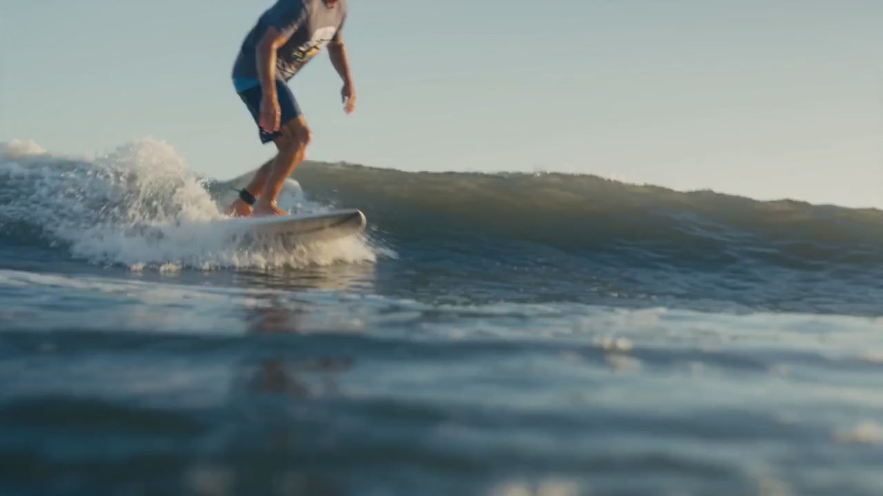 Load video: A surfer rides ocean waves, carving sharp turns and throwing spray under warm coastal light.