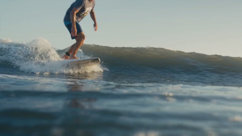 A surfer rides ocean waves, carving sharp turns and throwing spray under warm coastal light.