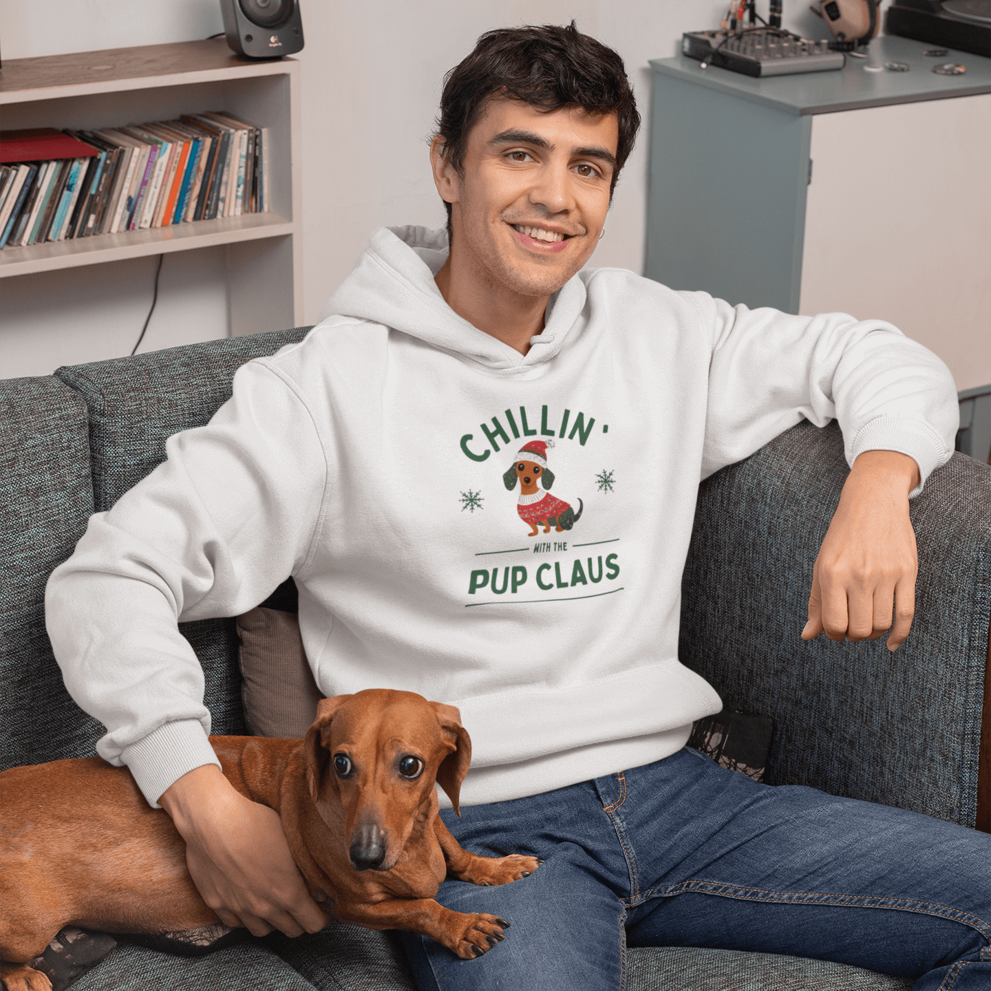 Man wearing 'Chillin' with Pup Claus' hoodie, relaxed fit with dog design, sitting on couch with a dog.