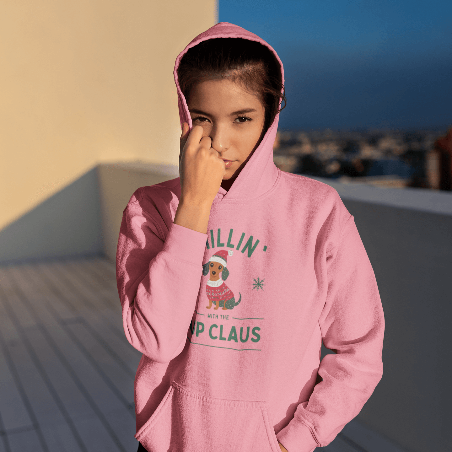 Young woman in pink hoodie with 'Chillin’ with Pup Claus' dog design, enjoying festive vibes outdoors.