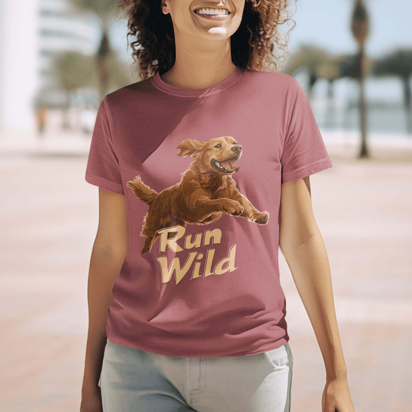 A smiling woman walking on a sunny street, wearing a T-shirt with a "Run Wild" design featuring a running Golden Retriever, symbolizing freedom and energy.