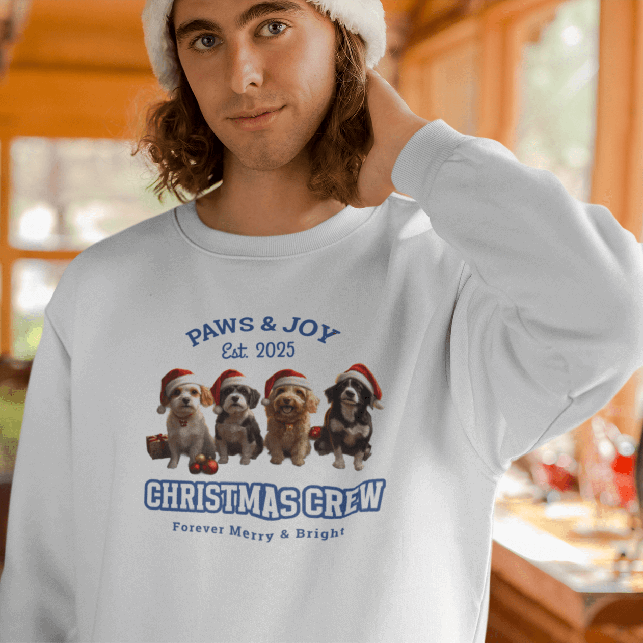 Man in a Santa hat wearing a white Christmas sweatshirt with "Christmas Crew" and dog illustrations, standing by a festive Christmas tree.