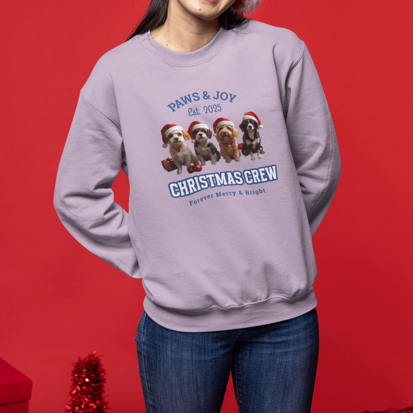 Woman wearing pink earmuffs and a purple Christmas sweatshirt with "Christmas Crew" and dog illustrations, standing against a red background, exuding a joyful holiday vibe.