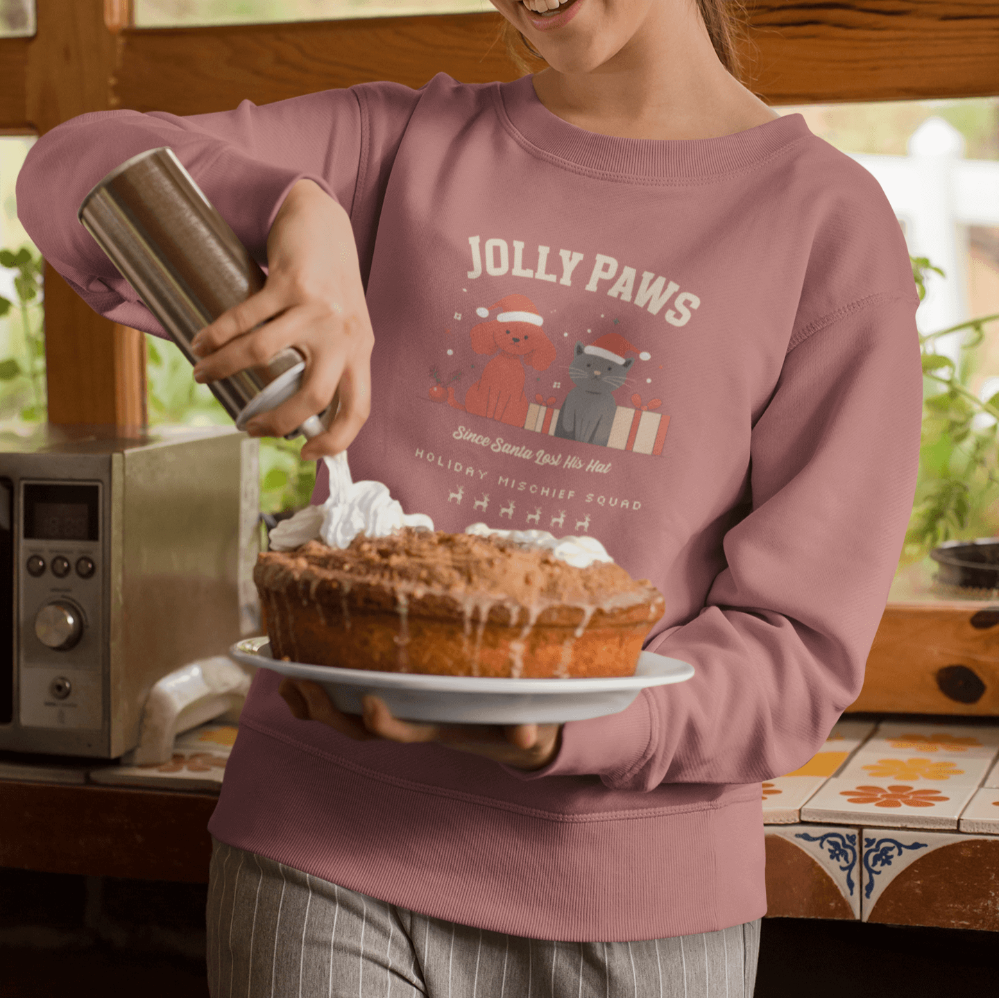 Woman wearing Jolly Paws sweatshirt while decorating a festive cake in a warm kitchen setting.