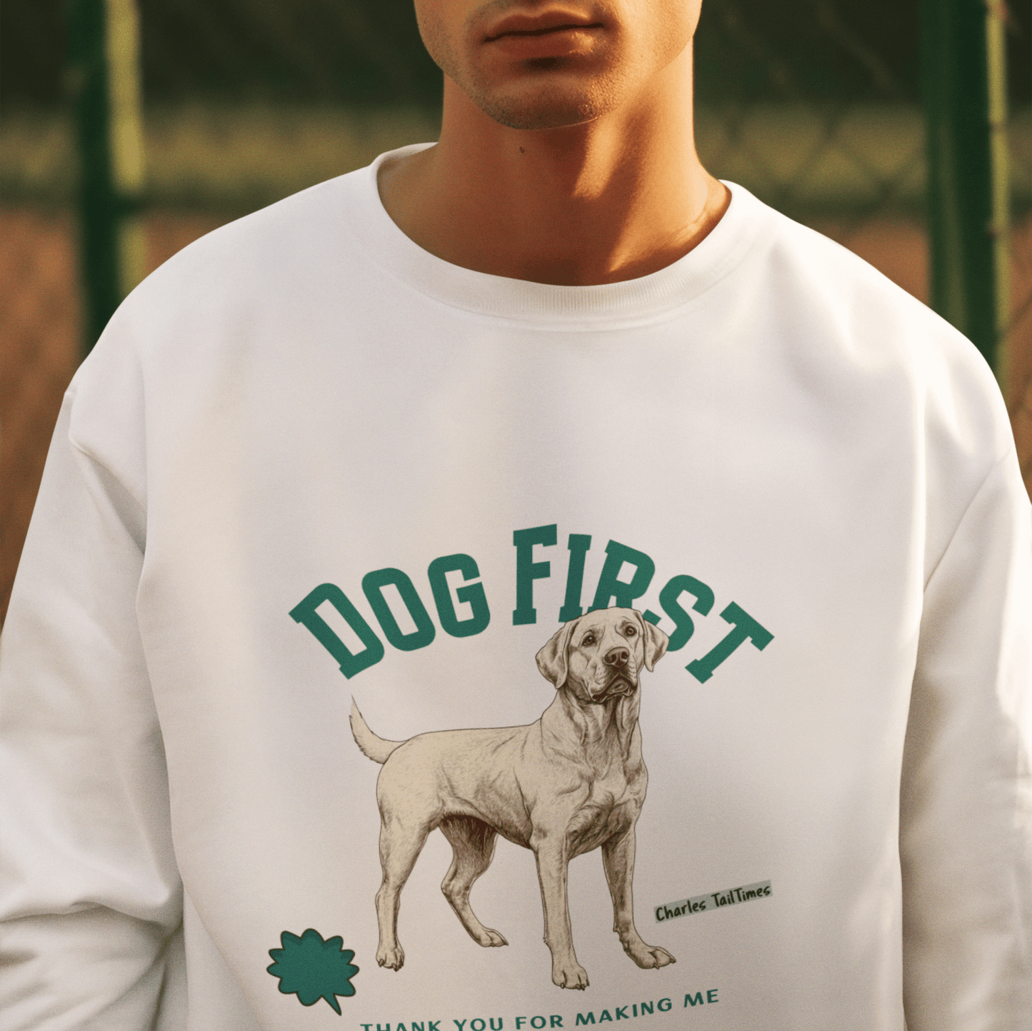 Male model wearing a white "Dog First" illustration sweatshirt featuring a Labrador design, set against a basketball court fence background.