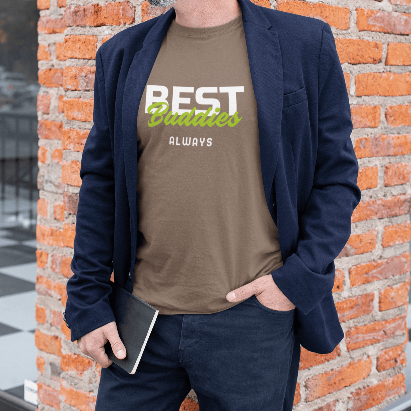 Middle-aged man wearing a brown T-shirt with the friendship-themed design "BEST Buddies ALWAYS," paired with a navy blazer, standing by a brick wall, exuding a casual yet stylish vibe.