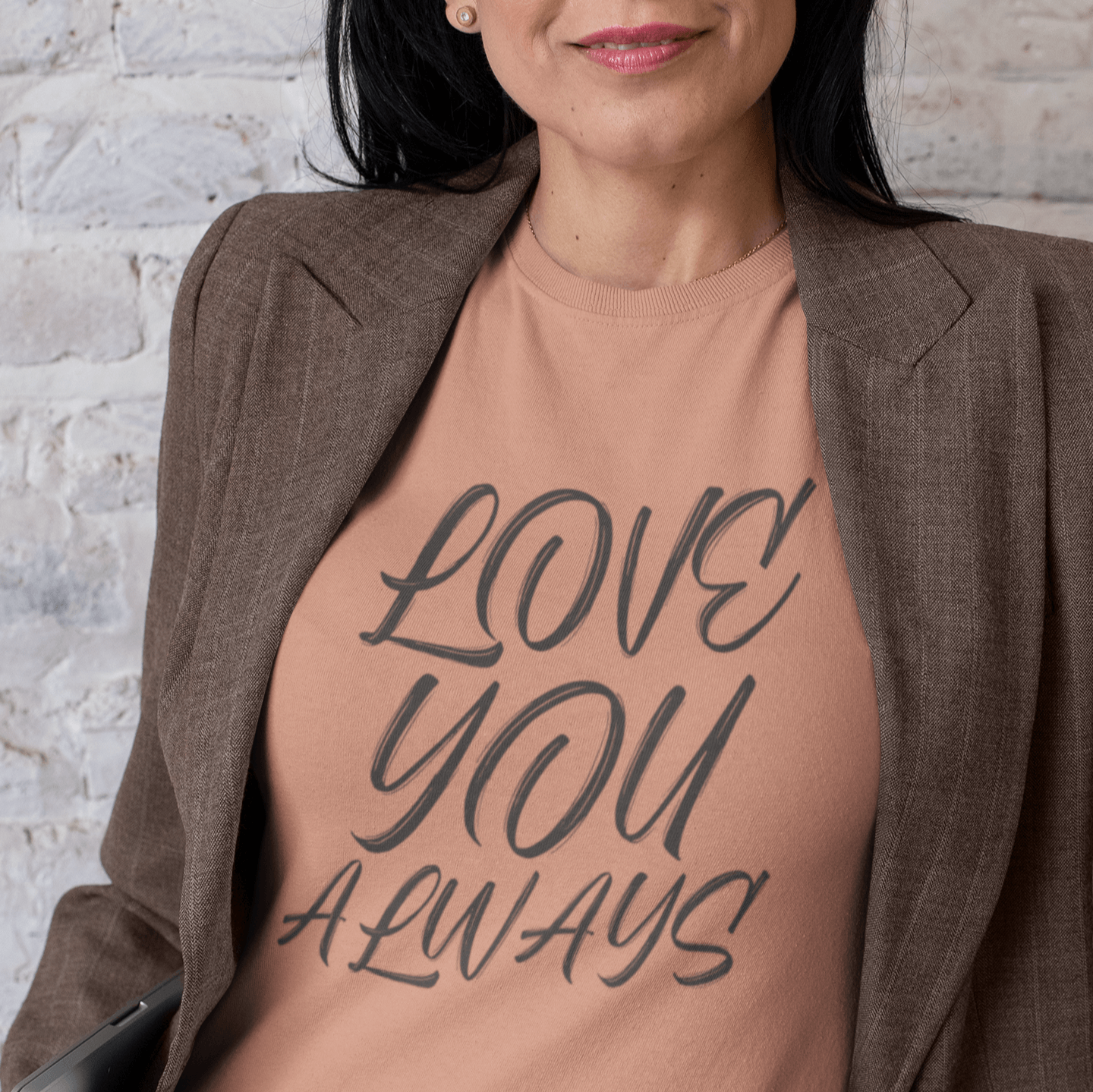 Woman wearing a peach-colored T-shirt with the handwritten text 'LOVE YOU ALWAYS' in dark gray, styled with a brown blazer.