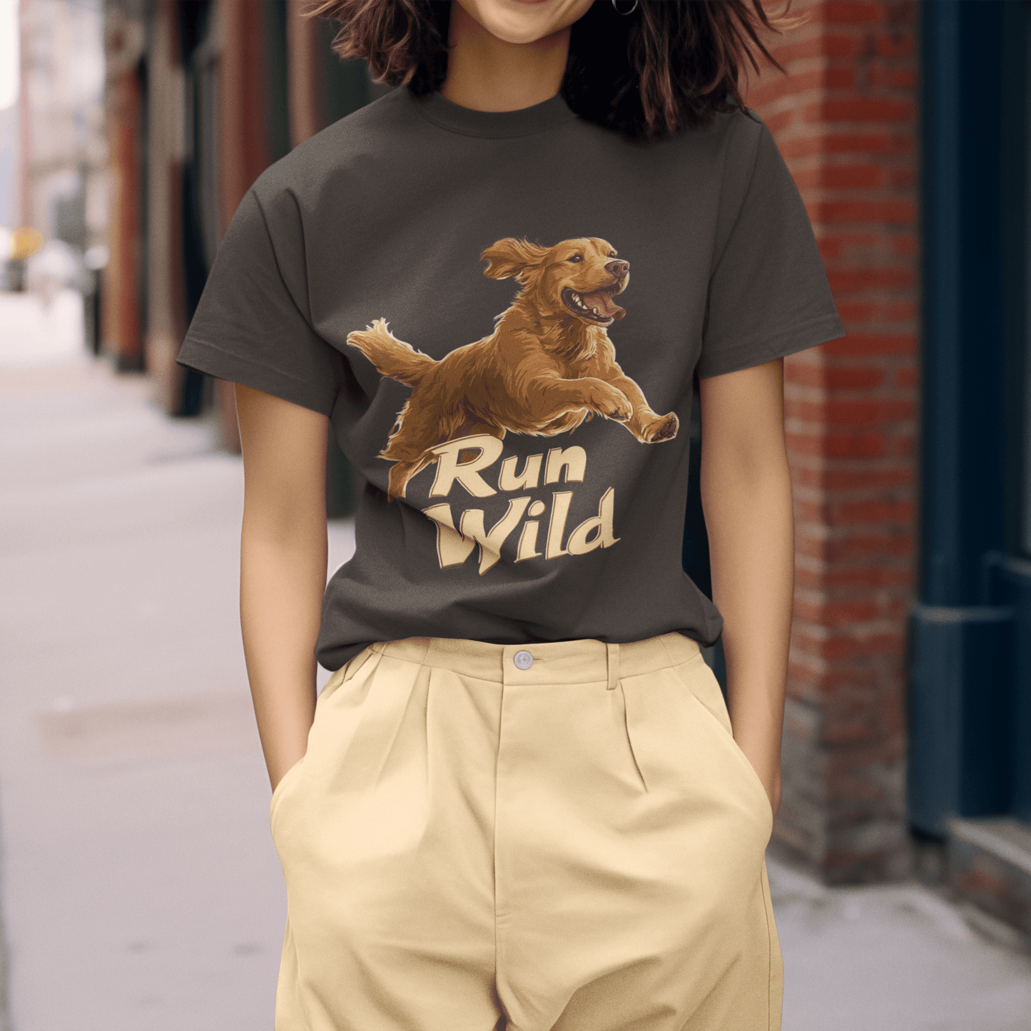 A woman wearing a T-shirt with a "Run Wild" graphic featuring a running Golden Retriever stands on an urban street. The design symbolizes freedom and energy.